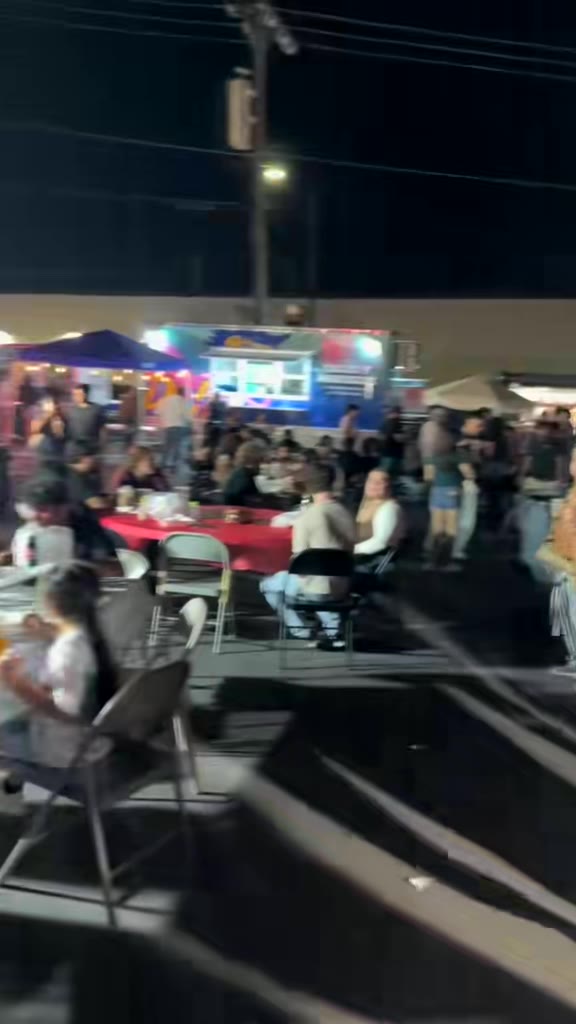 Crowded tables with red tablecloths in front of lit-up food trucks at night